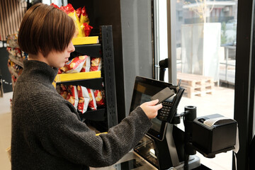 A woman pays with a contactless card at a self-checkout terminal in a supermarket. The concept highlights modern retail technology and convenient consumer experience.