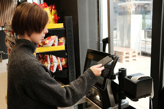 A woman pays with a contactless card at a self-checkout terminal in a supermarket. The concept highlights modern retail technology and convenient consumer experience.