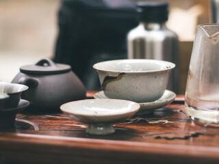 Close-up of rustic traditional gongfu ceramic tea bowls and a dark clay teapot arranged on an ornate wooden tray, evoking a calm, traditional tea ceremony atmosphere.