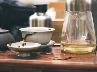 A glass pitcher of freshly brewed tea stands beside ceramic bowls and loose leaves on a carved wooden tray, illustrating the elegance of a gongfu tea session.