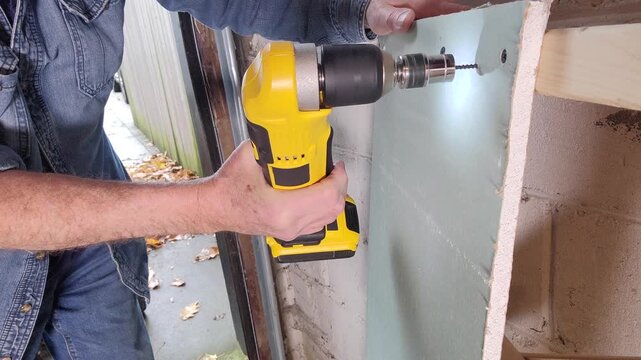 A worker using a cordless right angle drill to attach drywall to a stud wall