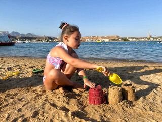 Young girl playfully building sandcastles by the beach, showcasing creativity and joy in a sunny coastal setting.