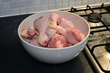 Raw chicken drumsticks in bowl on dark kitchen counter