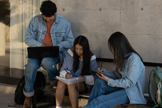 Diverse group of university students collaborating outdoors, using laptops, tablets, and notebooks for studying, learning, and sharing knowledge during a campus break
