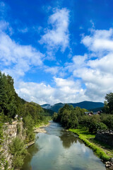 Sunny river landscape with green banks and blue sky in mountainous region