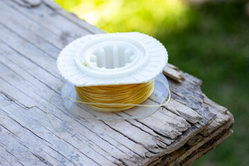 Spool of nylon fishing line. Fishing line on a rustic wooden table outdoors.Fishing and outdoor recreation concept. River sports. Fishing enthusiast gear.
