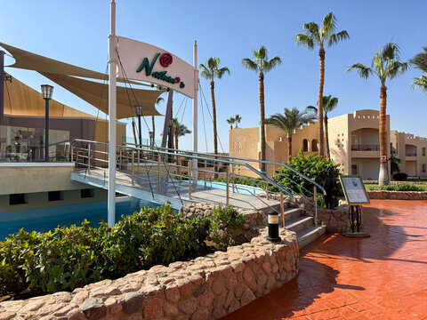 The entrance to the Neptuno Restaurant, a popular dining spot in a luxurious resort, framed by palm trees and clear blue skies.