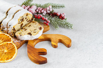 Traditional Christmas stollen, sweet fruit loaf sliced on wooden board, dusted with powdered sugar on white textured background, copy space. Spices, dried fruits and festive decor, winter holiday mood