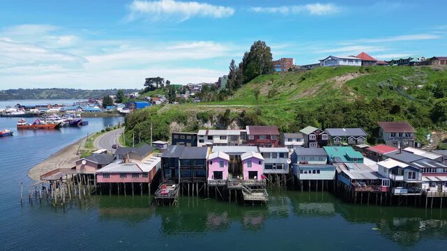 Castro, Chile: Backward aerial drone footage above colorful waterfront stilt houses in Castro in the idyllic Chiloe island, Lake District of Chile on a sunny day.