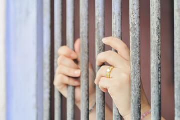 Obraz premium A pair of hands reaching through vertical steel bars of a jail or prison cell, with one hand wearing a pink beaded bracelet, symbolizing confinement, hope, despair, and freedom lost.