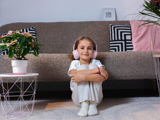 Young girl with headphones sitting on a cozy sofa, surrounded by decorative plants and modern furnishings, enjoying music in a stylish living room atmosphere