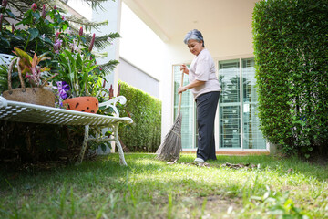 Senior woman sweeping backyard garden and cleaning outdoor area at home, Elderly woman doing outdoor chores and maintaining home garden, Active senior lifestyle with older woman cleaning yard