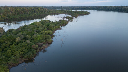 Sunset at Lake Valencia with warm orange light reflecting on calm Amazon waters, surrounded by the lush rainforest of Madre de Dios