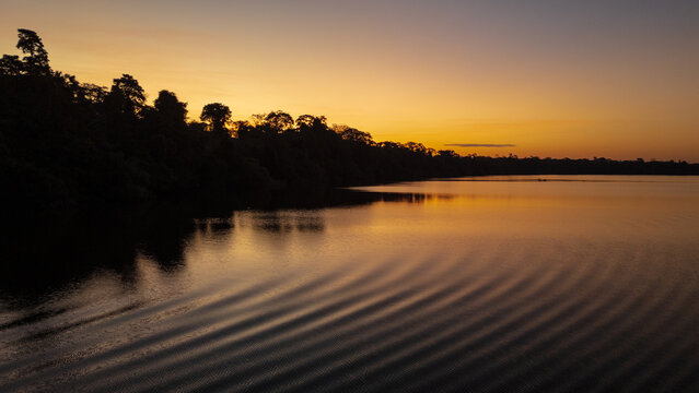 Sunset at Lake Valencia with warm orange light reflecting on calm Amazon waters, surrounded by the lush rainforest of Madre de Dios