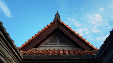 Closeup of a traditional balinese temples triangular roof structure with detailed terracotta tiles and stone elements against a clear blue sky, highlighting architectural beauty