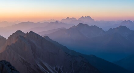Majestic mountain range with layers of peaks disappearing into the hazy morning mist during a beautiful, soft, and colorful sunrise