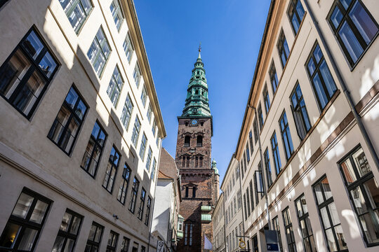 Nikolaj Kunsthallen, formerly the Nicholas church, red brick baroque clock tower with green spire on top against blue sky. - Powered by Adobe