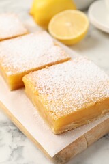 Tasty lemon bars with powdered sugar on white marble table, closeup