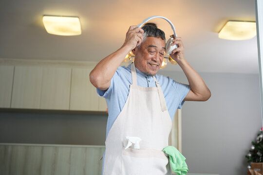 Senior man wearing headphones and getting ready for house cleaning at home, Elderly man enjoying music while preparing to do household chores indoors, Active senior lifestyle - Powered by Adobe