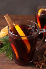 Tasty mulled wine in glass cup, spices and fir branches on wooden table against grey background, closeup