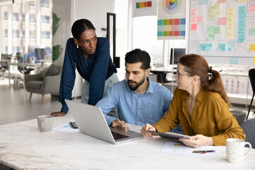 Multiethnic team of serious young colleagues talking at laptop