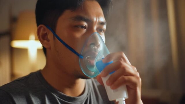 Close up of a man with COPD using a nebulizer for respiratory treatment indoors with soft lighting and a blurred background displaying curtains and a lamp