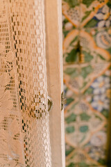 Delicate lace curtain partially drawn aside, revealing a colorful tiled wall in a cozy room