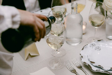 Wine is poured into a glass during an elegant dinner gathering at a beautifully set table in the evening