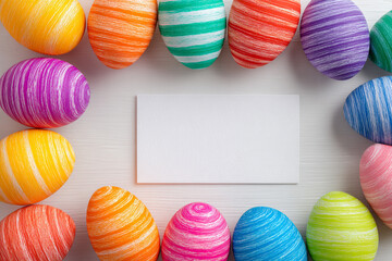 a frame of colorful striped easter eggs surrounding a blank white card on a light wood surface