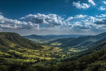 Naklejka premium Lush green rolling hills stretch towards distant blue mountains under a dramatic sky filled with white clouds
