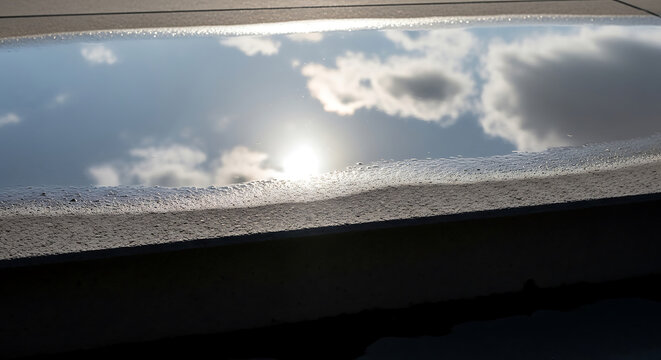 Cloud Reflection in Water Puddle on Flat Roof After Rain Storm Showing Sky Serenity