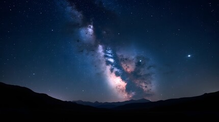 Fototapeta premium A spectacular long-exposure photograph of the Milky Way's vibrant galactic core and colorful nebula arching over a silhouetted mountain landscape at night