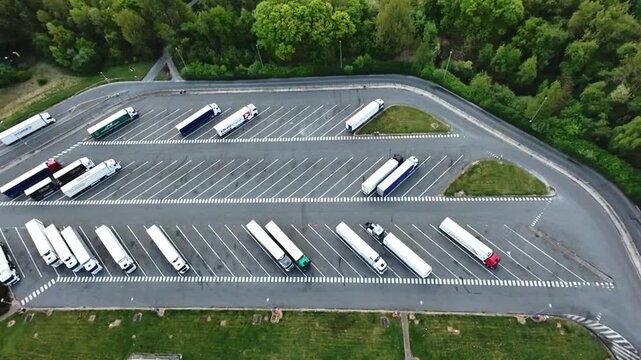 aerial view parked trailers by forest, neat rows in large lot, soft green backdrop, quiet pause between hauls, muted colors and calm atmosphere, logistics resting point beside trees