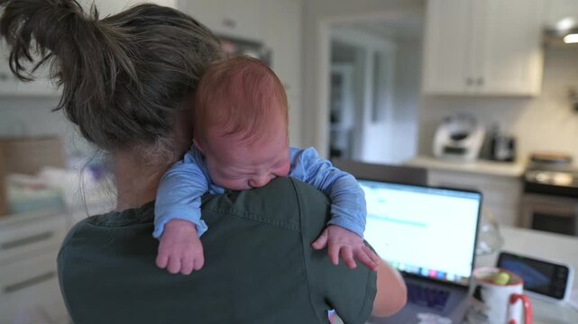 soothing infant amidst busy environment, mother tends to fussy baby as she balances job responsibilities, intimate domestic moment with mother soothing baby while managing professional tasks