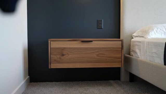 A wooden floating nightstand mounted on a dark blue painted wall