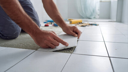 Tiler installing new bathroom floor tiles with meticulous care