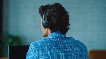 Man headset laptop home office video call remote work online meeting casual blue shirt curly hair. Man with headset laptop home office video call for remote work, online meeting casual blue shirt