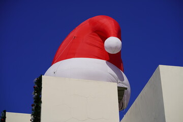 Large Inflatable Santa Hat Balloon Over Rooftop with Blue Sky Background Perfect for Holiday Decoration and Christmas Festivities