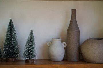 Minimalistic holiday decor featuring small artificial trees, ceramic vase, and unique pottery on...