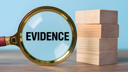 Magnifying glass focuses on the word evidence with wooden blocks stacked nearby against a blue background concept of investigation and proof examination process