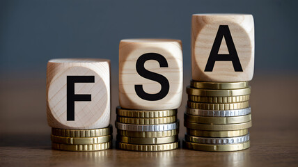 Wooden blocks spelling fsa on stacks of coins representing flexible spending account financial planning and savings for healthcare expenses and investment growth