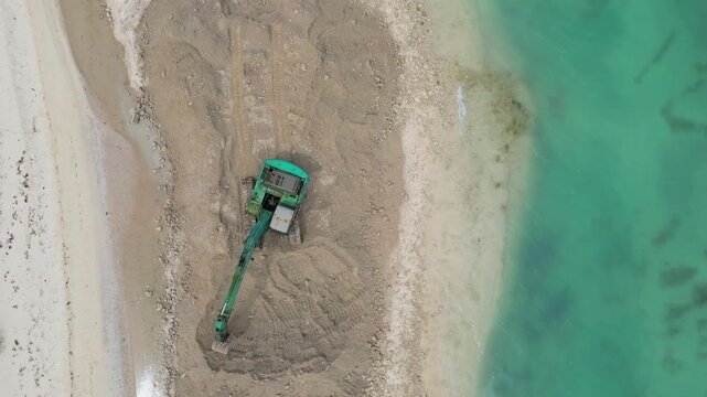 Aerial tracked excavator reshaping sandy coastline, green tracked machine digs and pushes sand to form
