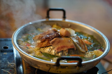 Traditional Hot Pot with Fresh Ingredients Cooking on a Stove with Rising Steam and Vibrant Vegetables and Meat Pieces in a Steel Pot