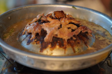 Delicious sizzling meat on a round grill with bubbling broth surrounded by fresh herbs in a vibrant dining setting, showcasing Asian culinary tradition