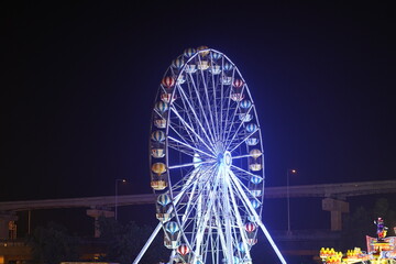 Nighttime view of a brightly illuminated Ferris wheel at an amusement park with vibrant lights and a clear dark sky in the background