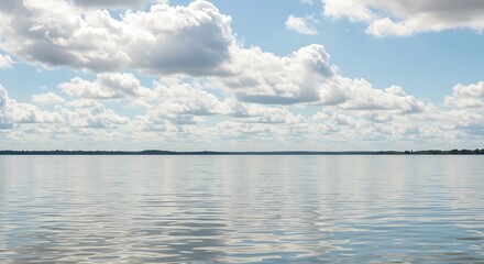 Obraz premium Calm water reflects a puffy cloud-filled sky under sunlight near a distant treeline