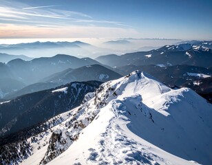 Aerial view of snowy mountain peaks under a hazy blue sky, distant ranges