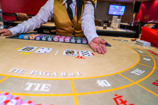 Baccarat dealer revealing cards on casino table, showing gambling decisions, risk, chance, strategy, luck and casino gaming atmosphere.