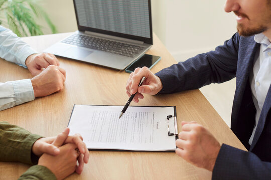 Couple sitting with male business broker or insurance agent showing documents sitting at the desk with laptop in office. Clients having consultation with man realtor or financial advisor.