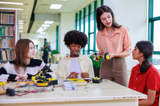 A group of diverse students works with a robotic arm alongside their teacher, showcasing hands-on STEM learning, teamwork, and modern classroom technology.